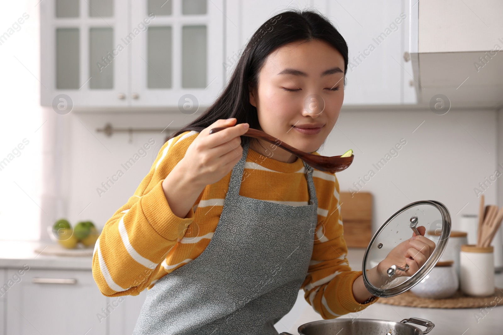 Photo of Beautiful woman cooking and tasting soup in kitchen