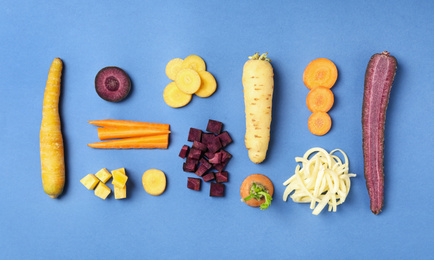 Photo of Whole and cut raw color carrots on blue background, flat lay