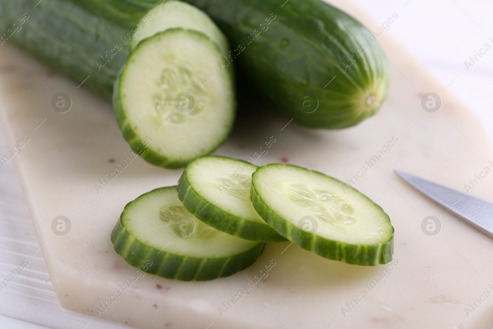 Photo of Cucumbers, knife and marble cutting board on white table, closeup