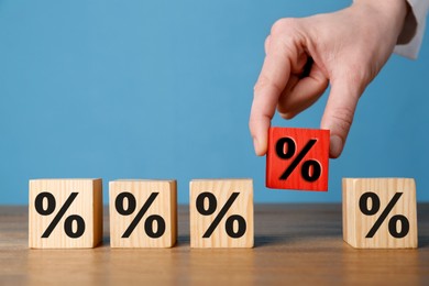 Image of Best mortgage interest rate. Woman putting red cube with percent sign among others on wooden table, closeup