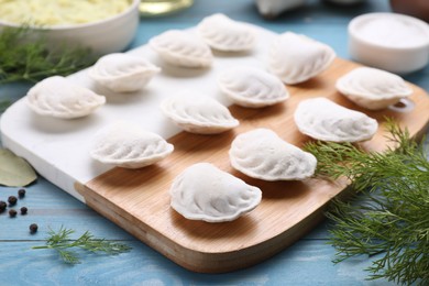 Photo of Raw dumplings (varenyky) and ingredients on light blue table, closeup