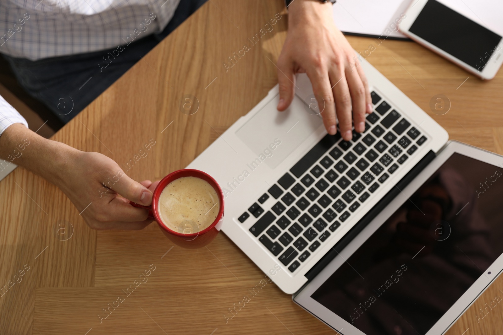 Photo of Man with cup of coffee and laptop at workplace, closeup