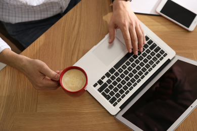Man with cup of coffee and laptop at workplace, closeup