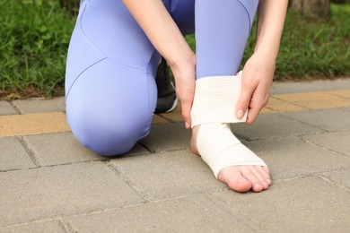 Photo of Woman wrapping foot in medical bandage outdoors, closeup