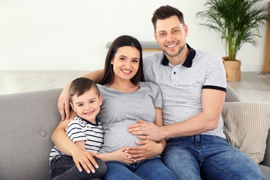 Photo of Father, son and pregnant mother spending time together on sofa at home. Family time