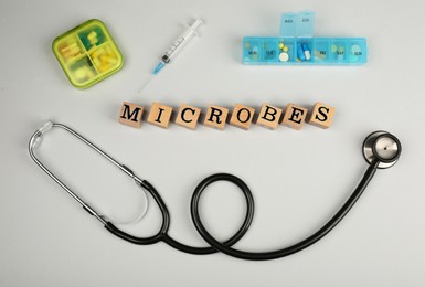 Photo of Word Microbes made with wooden cubes, pills and stethoscope on light background, flat lay