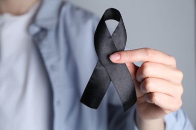 Photo of Woman holding black awareness ribbon on grey background, closeup