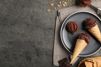 Photo of Chocolate ice cream scoops in wafer cones on gray textured table, flat lay. Space for text