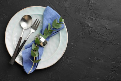 Stylish setting with cutlery, eucalyptus branch, napkin and plate on dark textured table, top view. Space for text