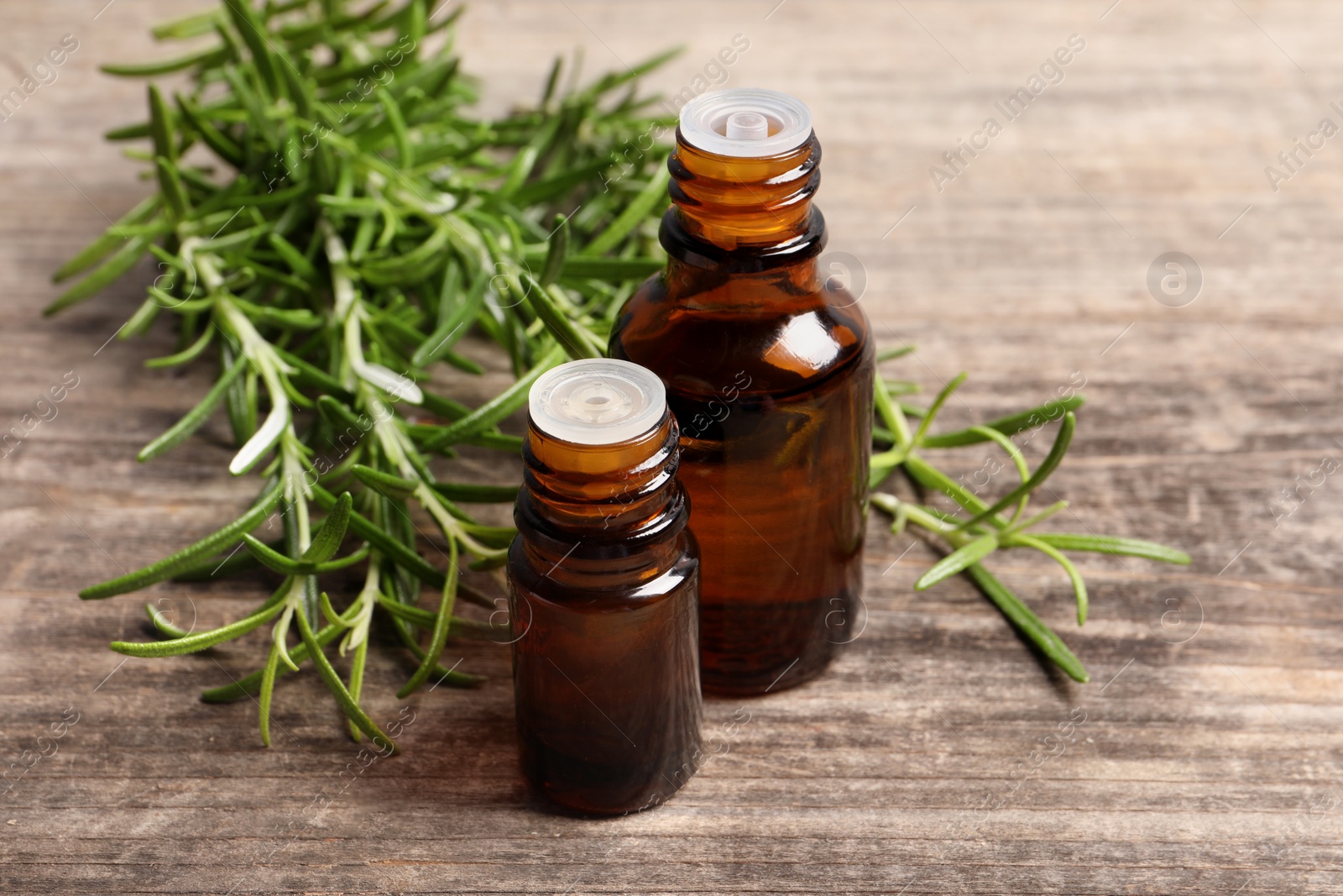 Photo of Bottles of essential oil and fresh rosemary sprigs on wooden table