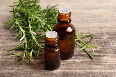 Photo of Bottles of essential oil and fresh rosemary sprigs on wooden table