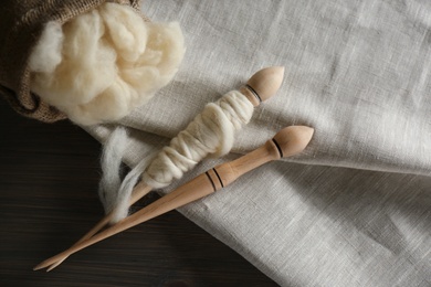 Photo of Soft white wool, spindles and fabric on wooden table, flat lay