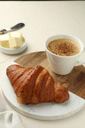 Photo of Tasty croissant served with cup of hot drink on light table, closeup