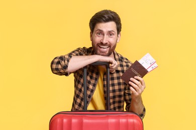 Smiling man with passport, tickets and suitcase on yellow background