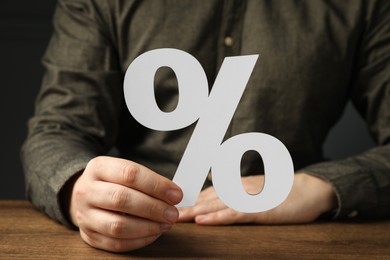 Photo of Man holding percent sign at wooden table, closeup