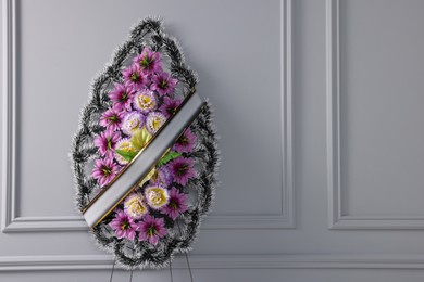 Photo of Funeral wreath of plastic flowers with ribbon near light grey wall, space for text