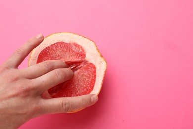 Woman touching half of grapefruit on pink background, top view and space for text. Sex concept