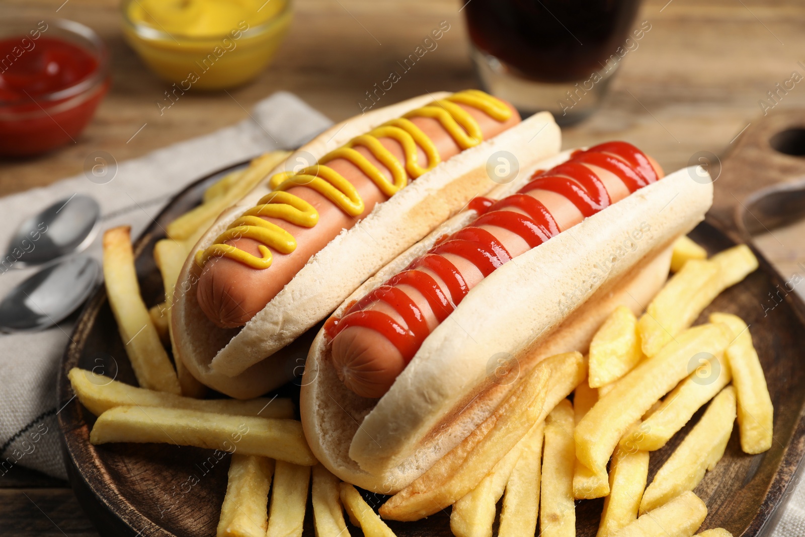 Photo of Delicious hot dogs with mustard, ketchup and potato fries on wooden table, closeup