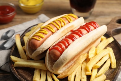 Delicious hot dogs with mustard, ketchup and potato fries on wooden table, closeup