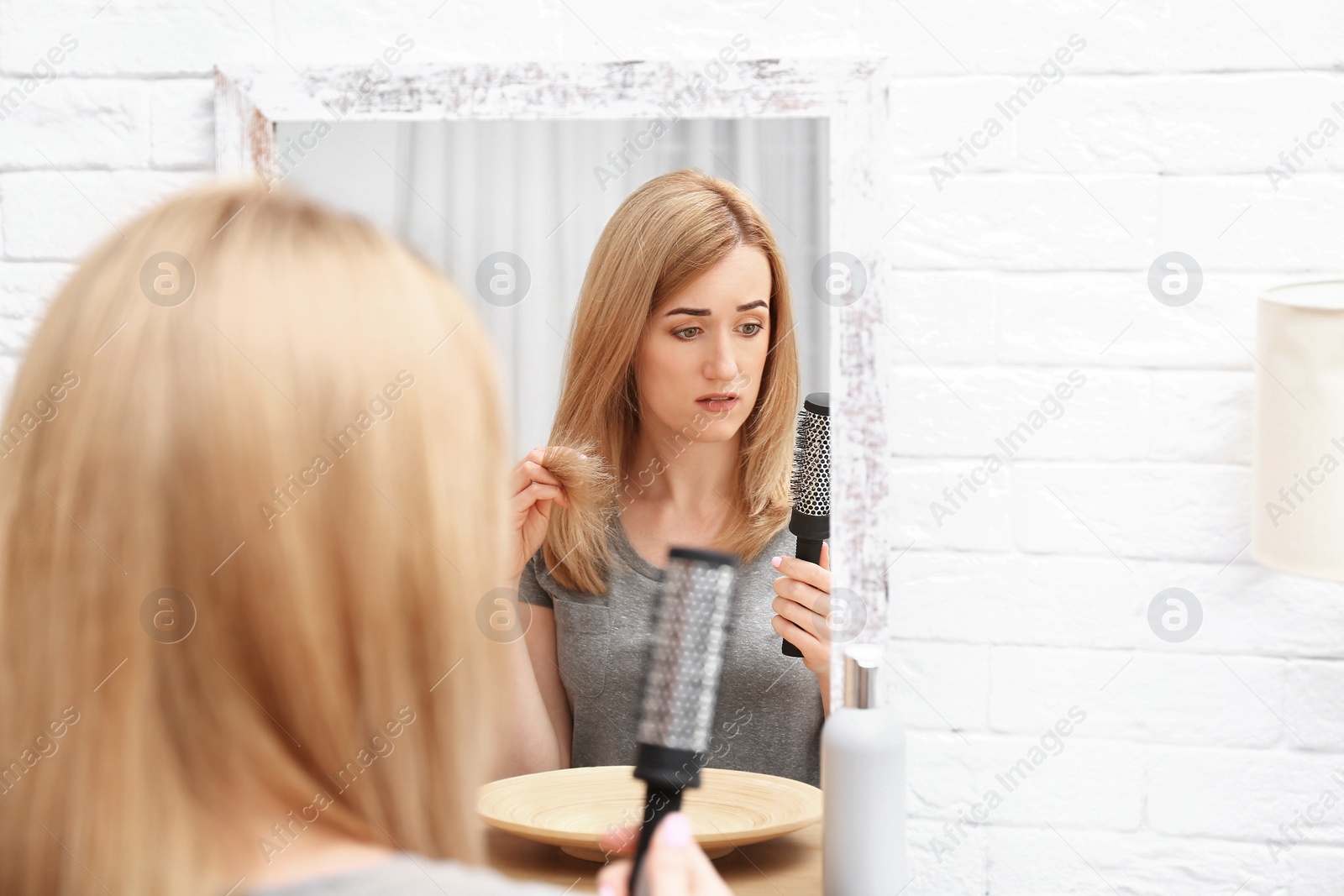 Photo of Emotional woman brushing hair near mirror in bathroom