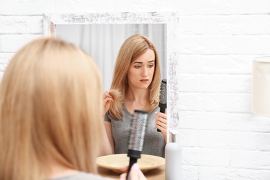 Photo of Emotional woman brushing hair near mirror in bathroom