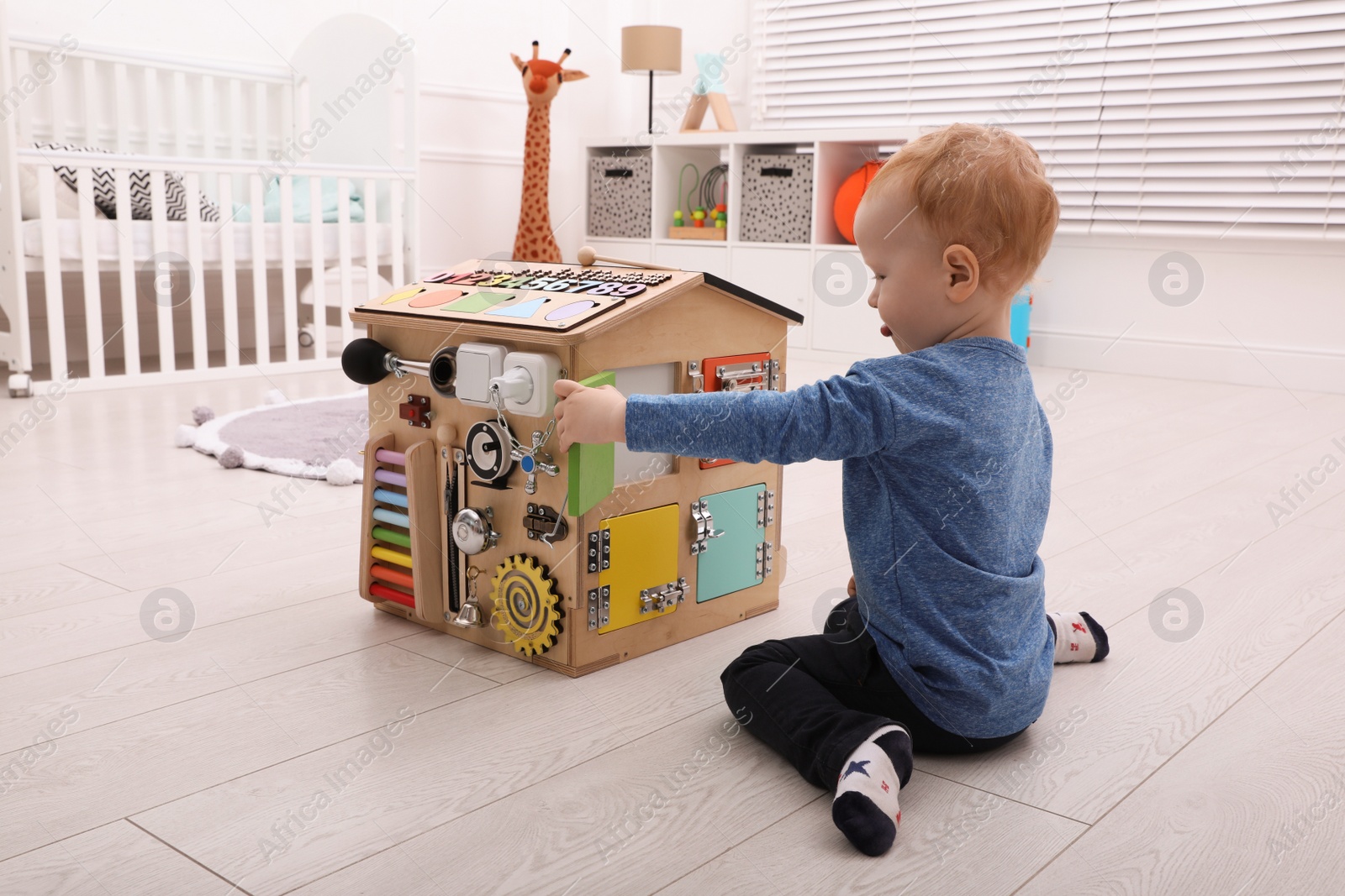 Photo of Cute little boy playing with busy board house on floor at home