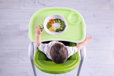 Photo of Cute little baby eating healthy food in high chair indoors, top view