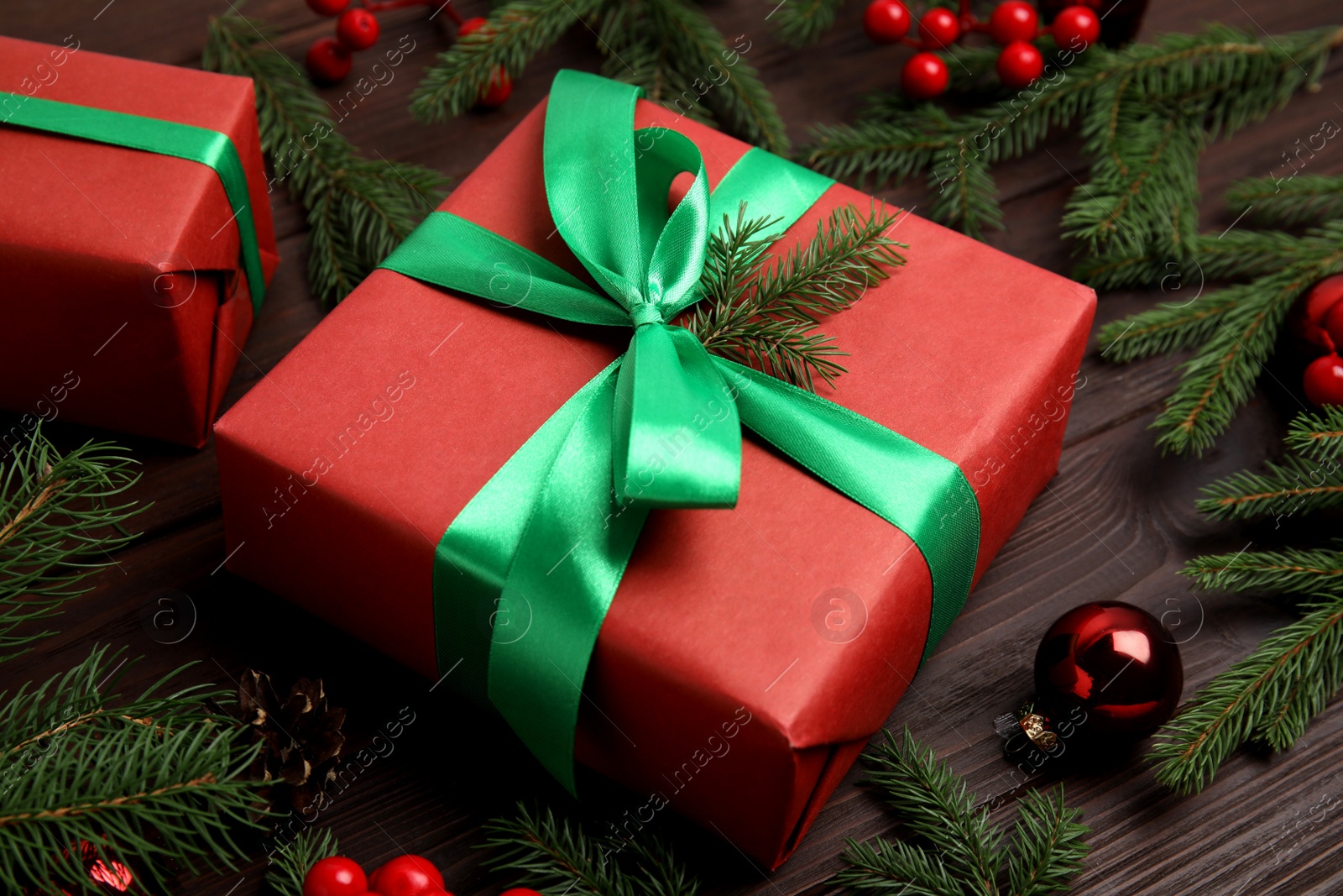 Photo of Red gift box with ribbon and Christmas decor on wooden table, closeup