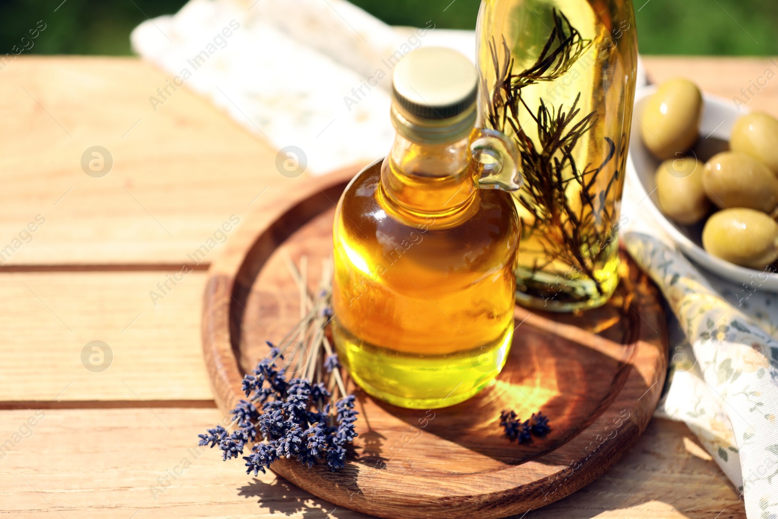 Photo of Different cooking oils and lavender flowers on wooden table against blurred green background, closeup