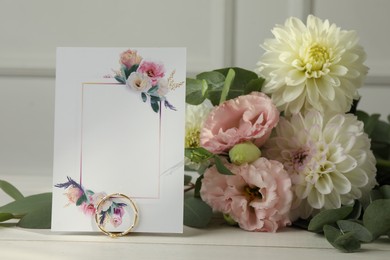 Photo of Blank invitation card, ring, eucalyptus leaves and flowers on white wooden table