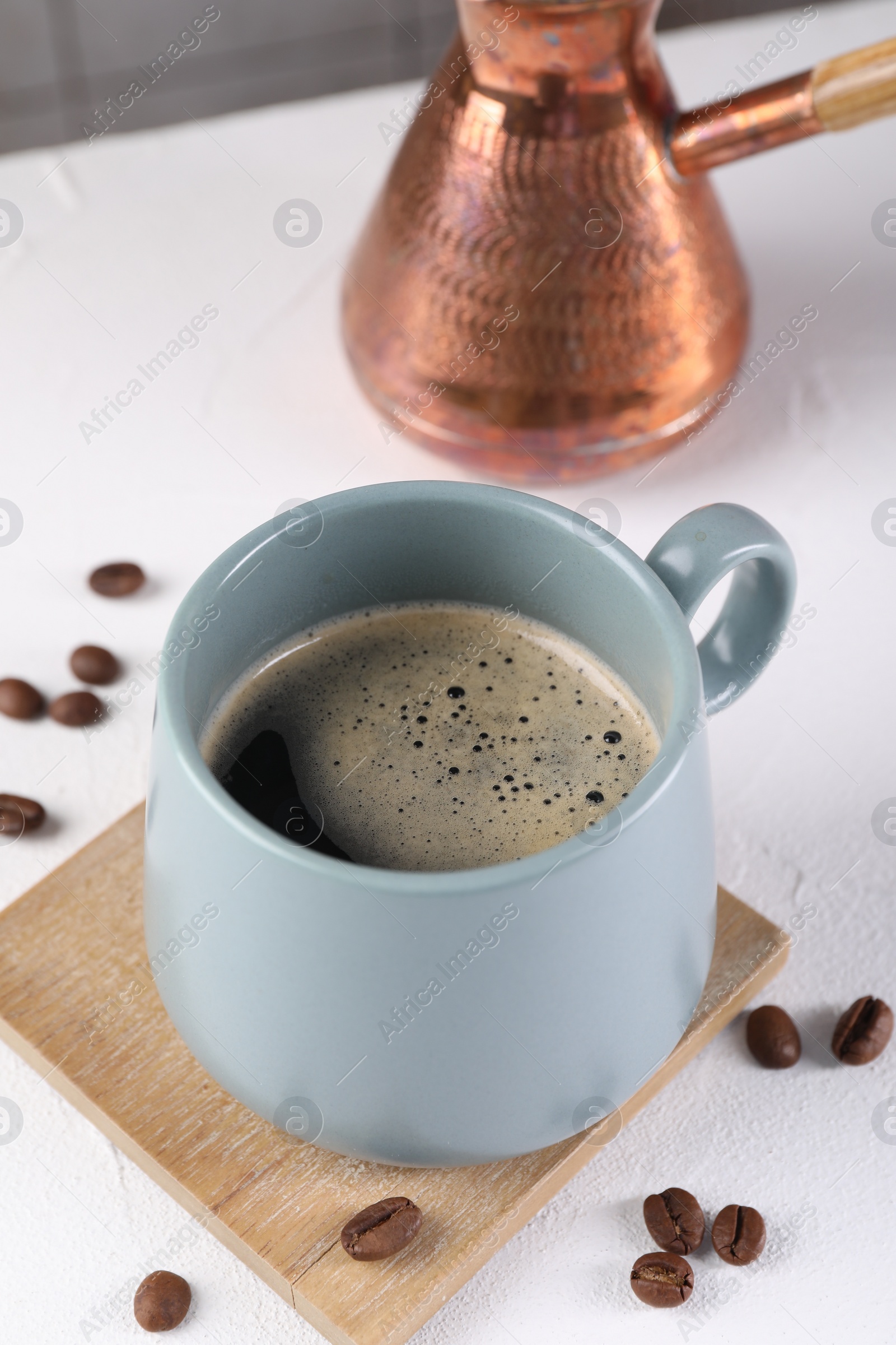 Photo of Delicious coffee in cup and beans on white textured table, closeup