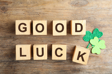 Photo of Cubes with phrase GOOD LUCK and clover leaves on wooden background, flat lay