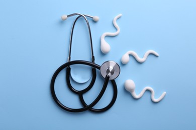 Photo of Reproductive medicine. Figures of sperm cells and stethoscope on light blue background, flat lay