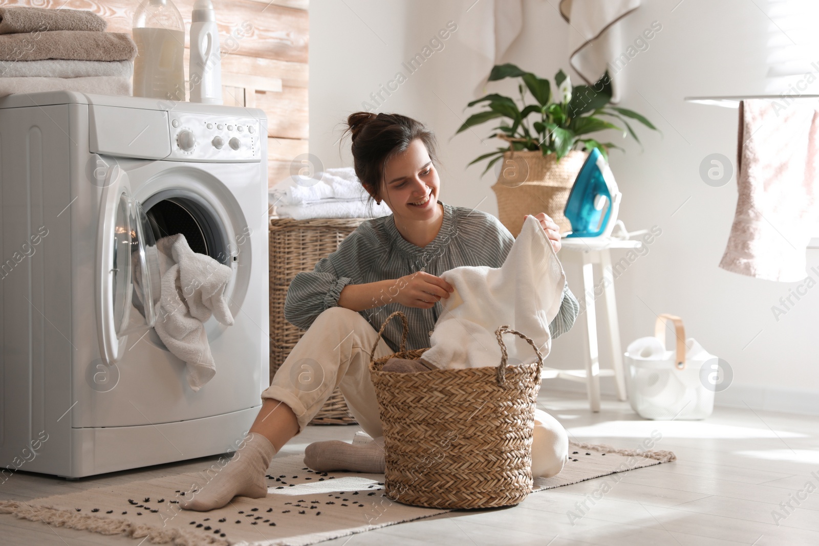 Photo of Young woman with laundry basket near washing machine at home