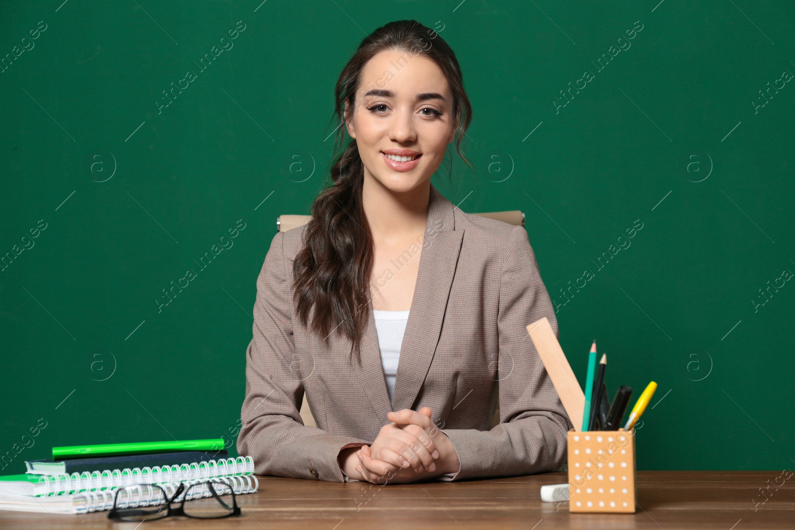 Photo of Portrait of beautiful young teacher sitting at table near chalkboard