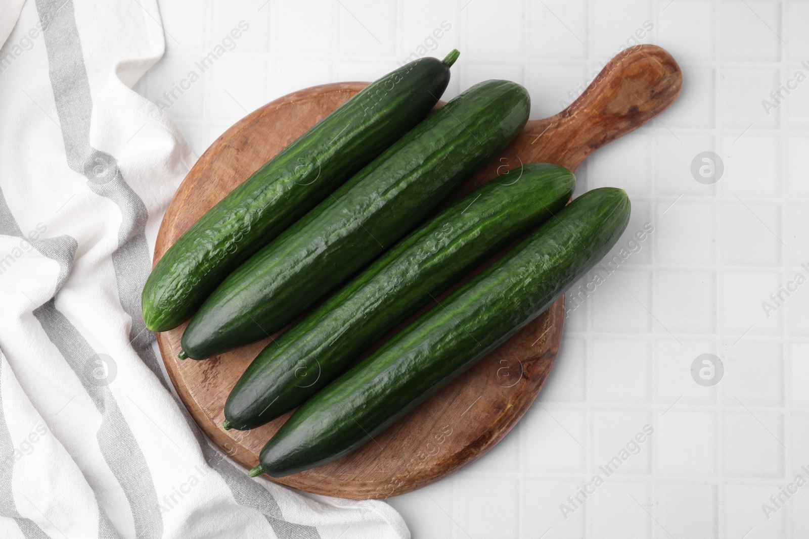 Photo of Fresh cucumbers on white tiled table, top view