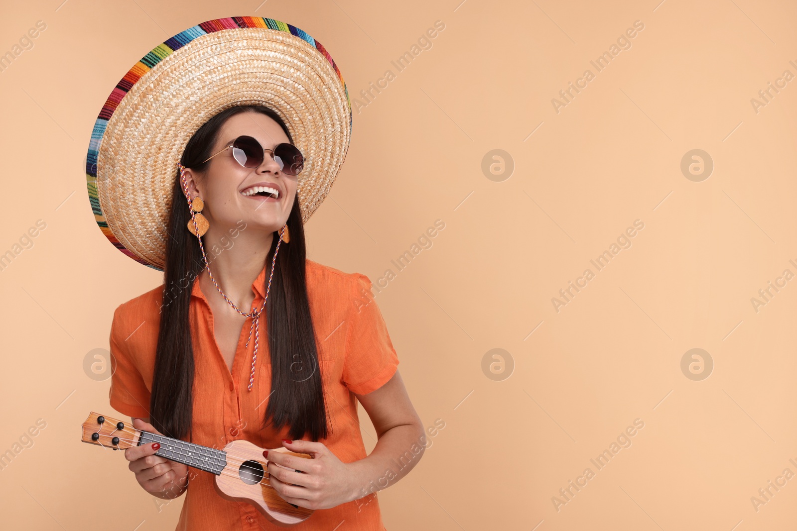 Photo of Young woman in Mexican sombrero hat playing ukulele on beige background. Space for text