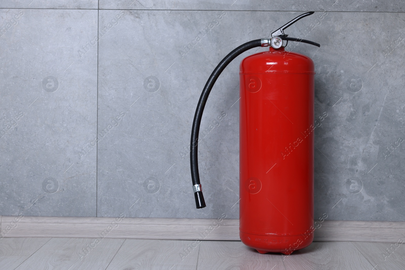 Photo of Fire extinguisher on floor near grey wall, space for text