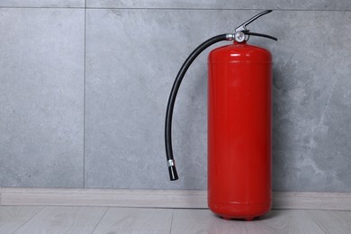 Photo of Fire extinguisher on floor near grey wall, space for text