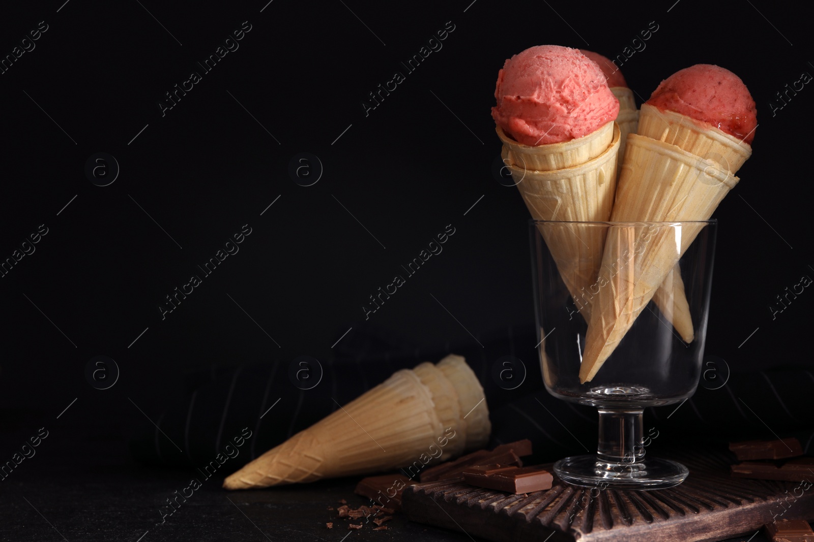 Photo of Delicious pink ice cream in wafer cones and chocolate  on black table. Space for text