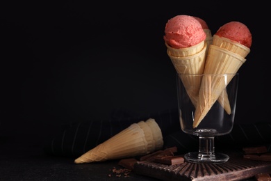 Photo of Delicious pink ice cream in wafer cones and chocolate  on black table. Space for text