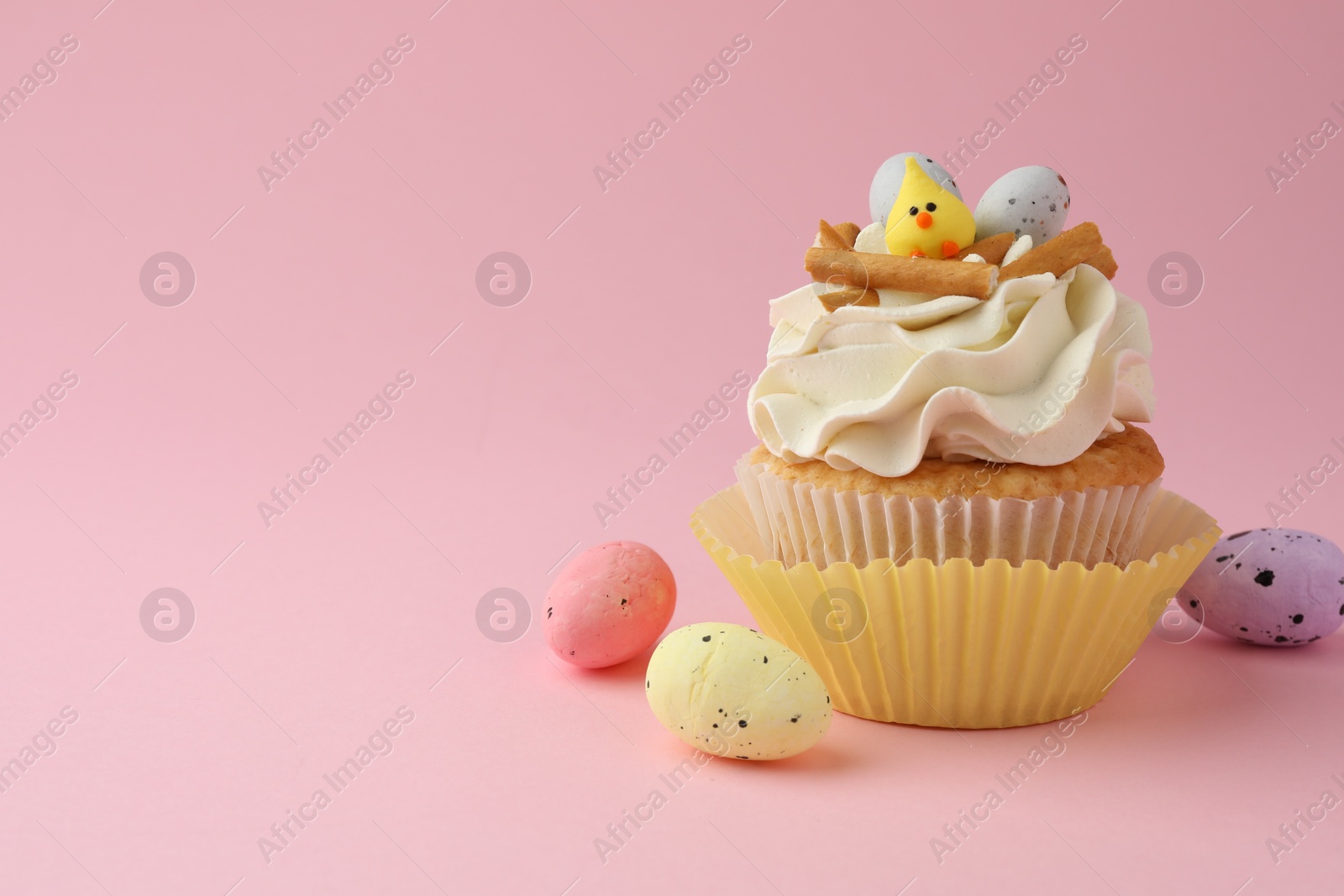 Photo of Tasty Easter cupcake with vanilla cream and candies on pink background, space for text