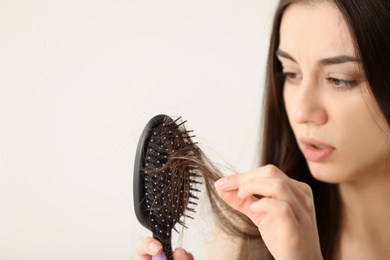Woman untangling her hair from brush on light background. Space for text