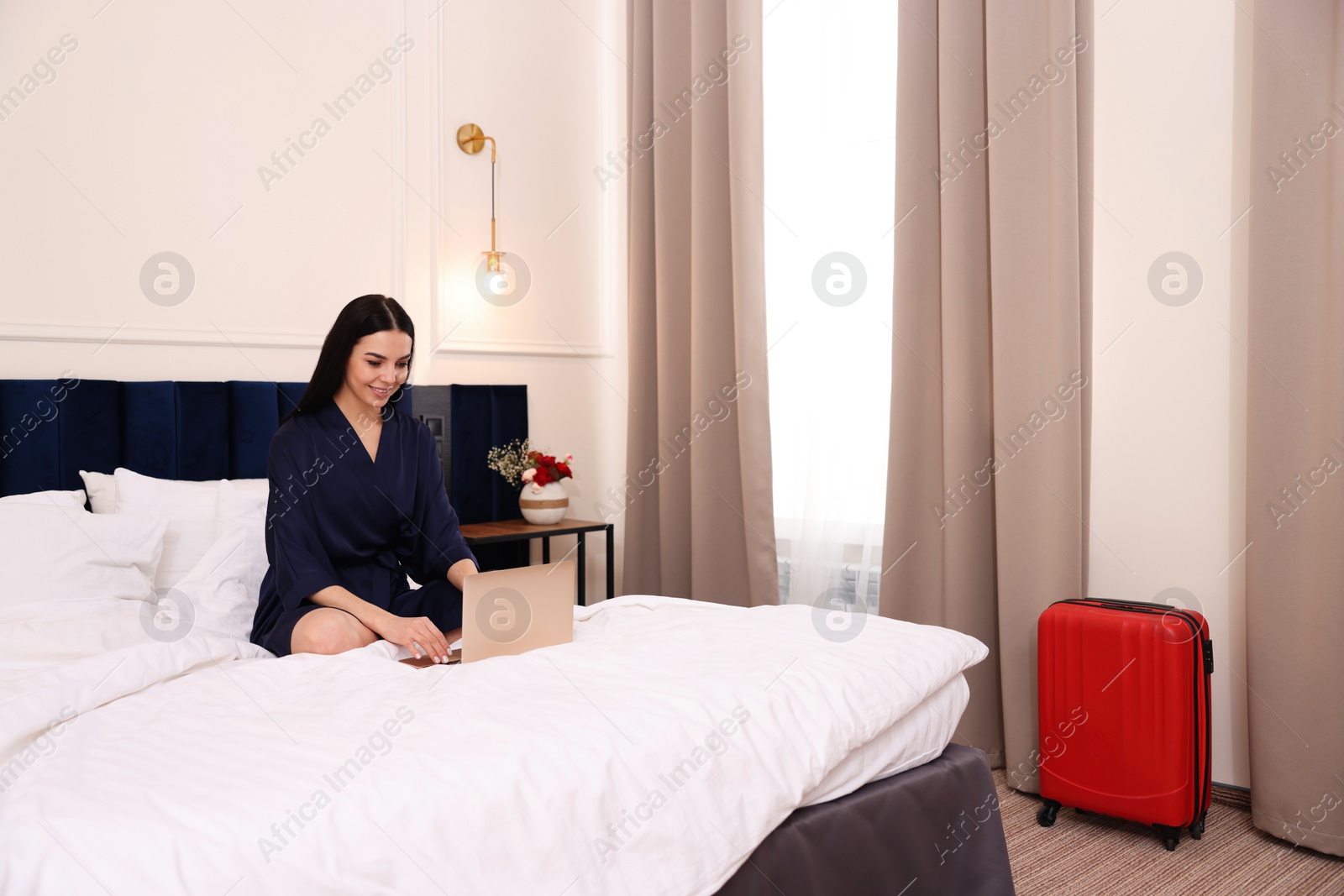 Photo of Beautiful young woman using laptop on bed in hotel room