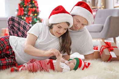 Photo of Happy couple with baby in Christmas hats at home