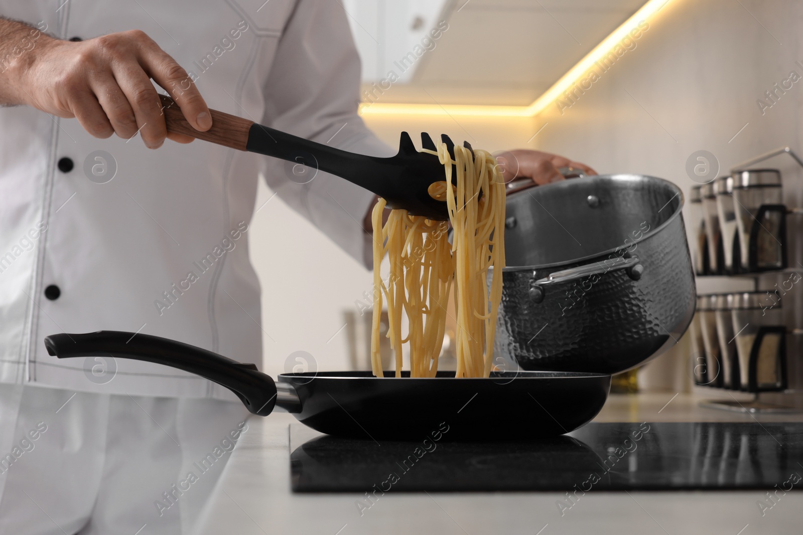 Photo of Professional chef cooking delicious pasta on stove in kitchen, closeup