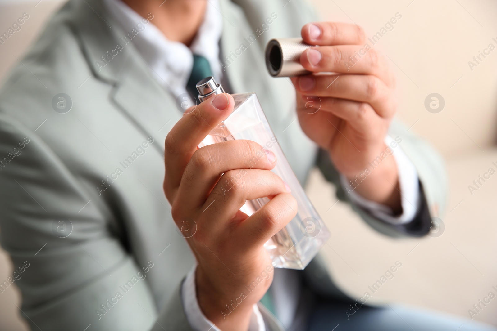 Photo of Businessman holding bottle of perfume on blurred background, closeup