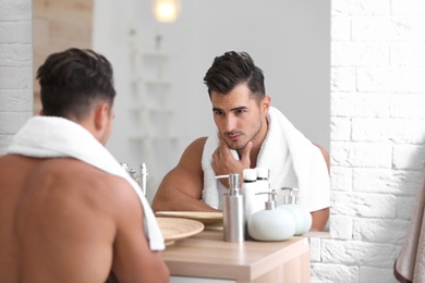 Young man with stubble ready for shaving near mirror in bathroom