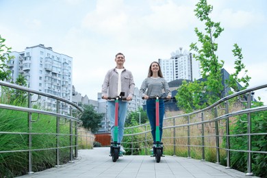 Photo of Happy couple riding modern electric kick scooters on city street