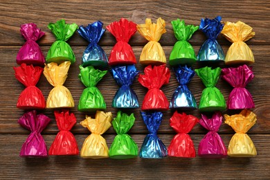 Photo of Many candies in colorful wrappers on wooden table, flat lay